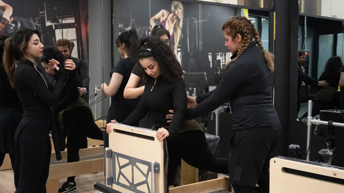 A group of people are engaged in a Pilates class, utilizing specialized equipment and mirrors to observe their movements.