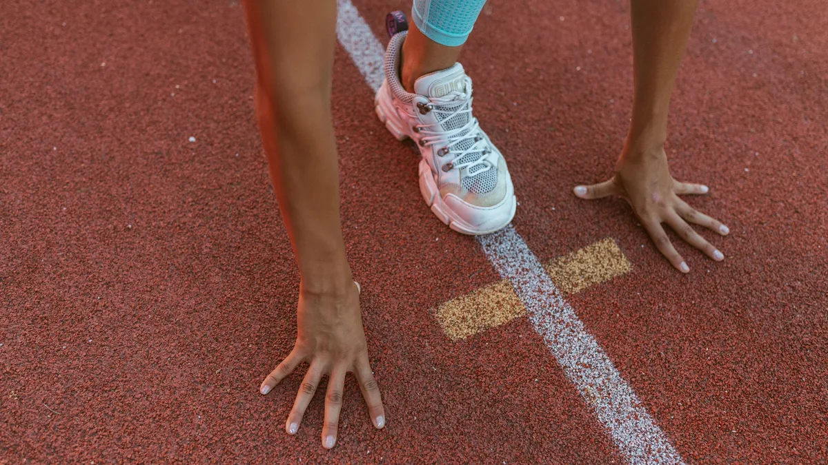 A person's hands and feet on a running track, with their hands on the ground and their feet on the starting line.