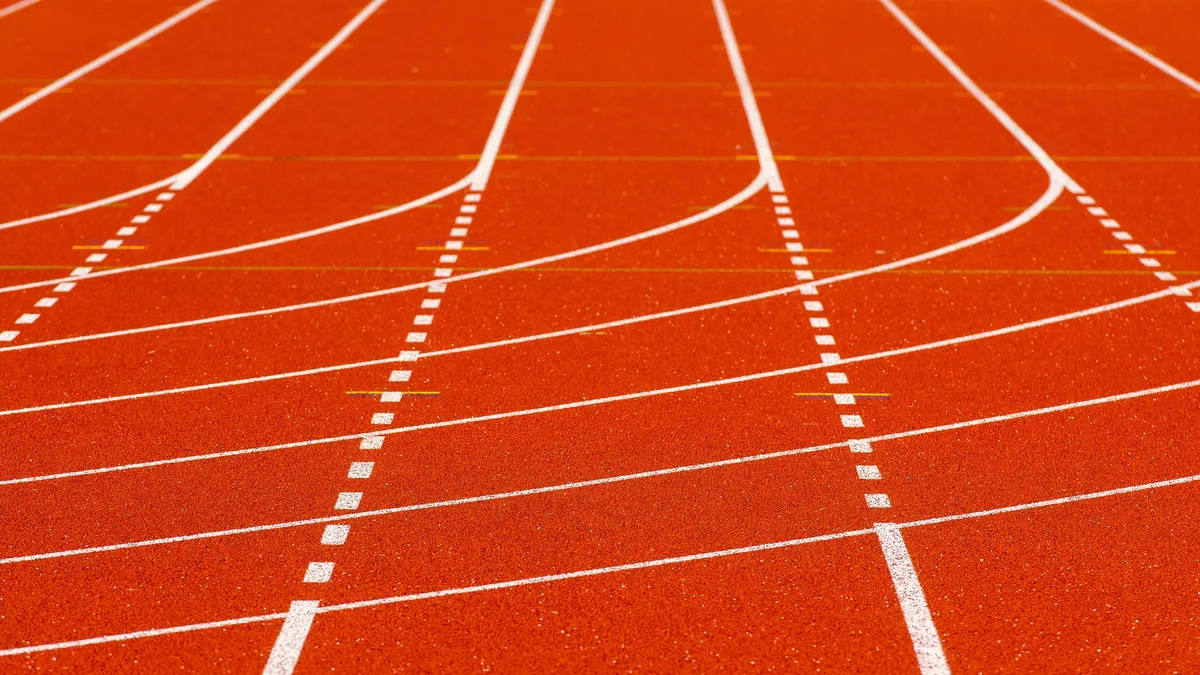 A red running track with white lines and markings, including lanes, starting blocks, and a finish line.